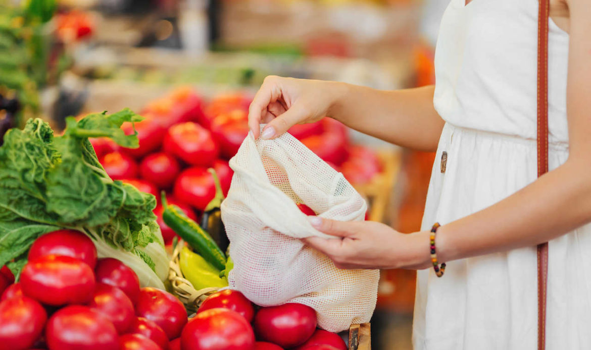 mulher coloca tomantes dentro de uma sacola em um supermercado
