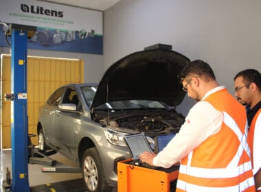 alt=homens com coletes laranjas dentro de uma oficina mecânica utilizam o scanner em um carro