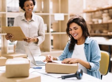 Happy young businesswoman sticking a barcode label on a package box. Online store owners preparing an order for shipping in a warehouse. Female