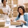 Happy young businesswoman sticking a barcode label on a package box. Online store owners preparing an order for shipping in a warehouse. Female